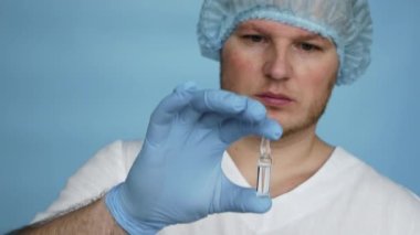 Ağır çekimde, steril eldiven giymiş sabahlık giymiş bir doktor ilacı ampulde gösteriyor. Ampulde sıvı ilaç tedavisi. Erkek eczacı..