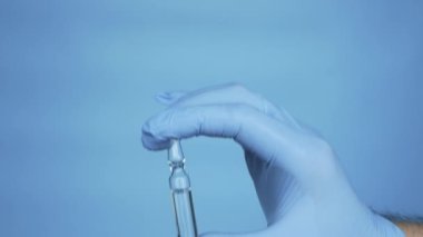 Doctor's hands in rubber medical mittens and an ampoule. A man demonstrates medicine in a medical ampoule. Treatment liquid medicine in an ampoule. Male worker pharmacist