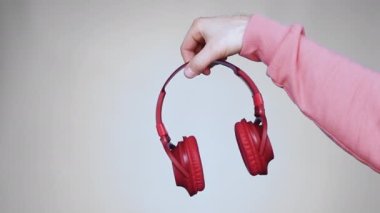 Gri bir stüdyonun arka planında genç bir adamın elindeki müzik kulaklıkları. Ağır çekim. Kırmızı başlıklı müzik kulaklıkları bir erkeğin elini tutuyor.