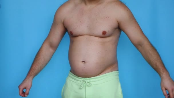 大きな脂肪の腹を持つ脂肪の男は 青いスタジオの背景に 筋肉を示しています大きな腹を持つ脂肪の男は 両足を示しています 肥満の人々 減量の概念 — ストック動画