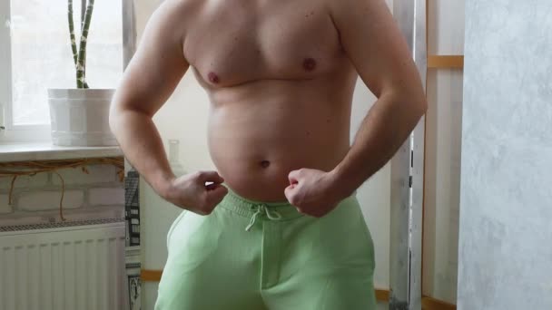 たるんだ肌をした筋肉のない太った男 太った男が鏡の前にポーズをとる 男は体の筋肉を見て 脂肪1と面白いビデオ 肥満の人 — ストック動画