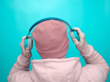 Turkuazlı genç bir adam, stüdyo arka planında naneli müzik kulaklıkları. Kapüşonlu ve kulaklıklı, en sevdiği müziği dinleyen mutlu adam. Tarz sahibi bir adamla müzik geçmişi.