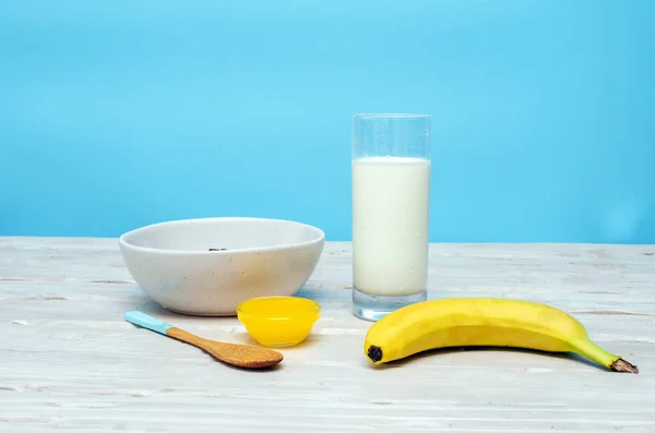 一杯牛奶和香蕉 还有意大利面和蜂蜜 在一张蓝色背景的木制桌子上 — 图库照片
