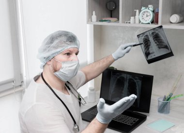 Profesyonel bir doktor hastasına teşhis koyar, ofiste oturur ve akciğerleri bilgisayarda analiz eder. Hastalık tüberküloz. Hastanede ya da klinikte çalışan bir doktor, akciğerlerin zatürreesini dikkatlice analiz eder..