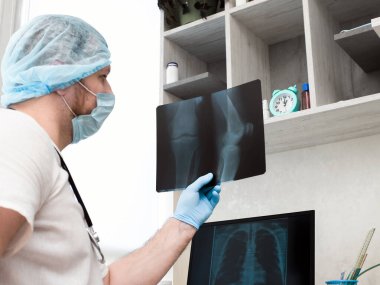 Doktor radyograf, steteskopla klinikte tıbbi üniformayla kırık bir bacağı analiz ediyor. Dizinin röntgeni. Ultrason. Diz ekleminde bacak yaralanması. Kemik erimesi