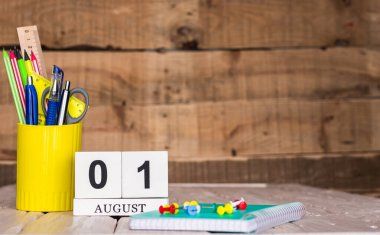 Ağustos takvim arkaplanı 1 numara. Ahşap bir arka planda bir çantada kırtasiye kalemleri ve kalemler. Yer defterini kalem ve takvimle kopyala. Metin için planlayıcı yer.