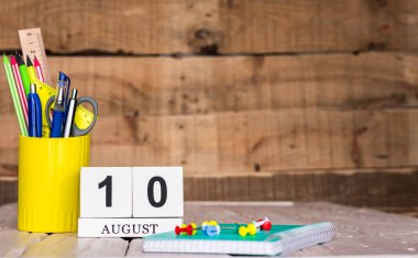 Ağustos takviminde 10 numara var. Ahşap bir arka planda bir çantada kırtasiye kalemleri ve kalemler. Yer defterini kalem ve takvimle kopyala. Metin için planlayıcı yer.