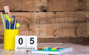 Eylül takviminde 5 numara var. Ahşap bir arka planda bir çantada kırtasiye kalemleri ve kalemler. Yer defterini kalem ve takvimle kopyala. Metin için planlayıcı yer.