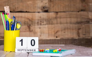 Eylül takviminde 10 numara var. Ahşap bir arka planda bir çantada kırtasiye kalemleri ve kalemler. Yer defterini kalem ve takvimle kopyala. Metin için planlayıcı yer.