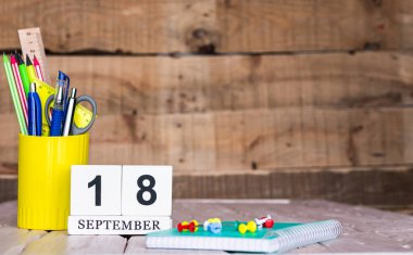 Eylül takviminde 18 numara var. Ahşap bir arka planda bir çantada kırtasiye kalemleri ve kalemler. Yer defterini kalem ve takvimle kopyala. Metin için planlayıcı yer.