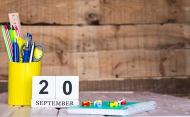 Eylül takviminde 20 numara var. Ahşap bir arka planda bir çantada kırtasiye kalemleri ve kalemler. Yer defterini kalem ve takvimle kopyala. Metin için planlayıcı yer.