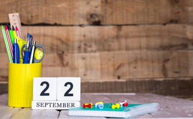 Eylül takviminde 22 numara var. Ahşap bir arka planda bir çantada kırtasiye kalemleri ve kalemler. Yer defterini kalem ve takvimle kopyala. Metin için planlayıcı yer.