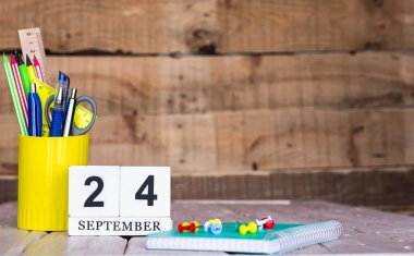 Eylül takviminde 24 numara var. Ahşap bir arka planda bir çantada kırtasiye kalemleri ve kalemler. Yer defterini kalem ve takvimle kopyala. Metin için planlayıcı yer.