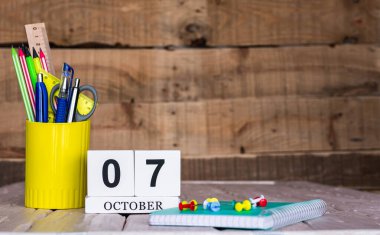 Ekim takviminde 7 numara var. Ahşap bir arka planda bir çantada kırtasiye kalemleri ve kalemler. Yer defterini kalem ve takvimle kopyala. Metin için planlayıcı yer.