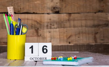 Ekim takviminde 16 numara var. Ahşap bir arka planda bir çantada kırtasiye kalemleri ve kalemler. Yer defterini kalem ve takvimle kopyala. Metin için planlayıcı yer.