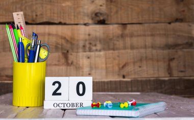 Ekim takviminde 20 numara var. Ahşap bir arka planda bir çantada kırtasiye kalemleri ve kalemler. Yer defterini kalem ve takvimle kopyala. Metin için planlayıcı yer.