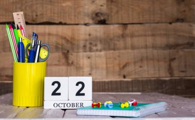 Ekim takviminde 22 numara var. Ahşap bir arka planda bir çantada kırtasiye kalemleri ve kalemler. Yer defterini kalem ve takvimle kopyala. Metin için planlayıcı yer.