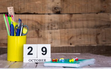 Ekim takviminde 29 numara var. Ahşap bir arka planda bir çantada kırtasiye kalemleri ve kalemler. Yer defterini kalem ve takvimle kopyala. Metin için planlayıcı yer.