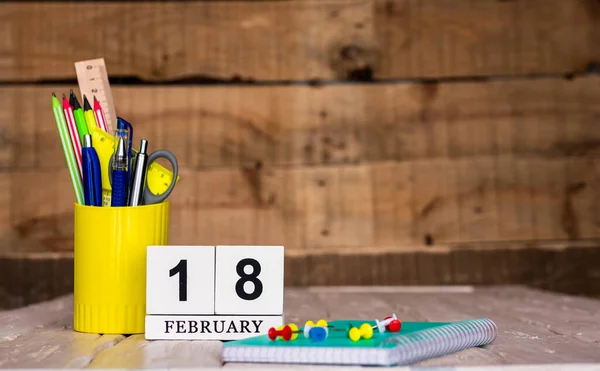 February calendar background with number  18. Stationery pens and pencils in a case on a wooden vintage background. Copy space notepad with pencils and calendar. Planner place for text.