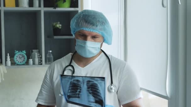 戴着医疗面罩和无菌手套的医生用X光检查病人的肺部 结论肺炎 医生在医院与听诊器 医生手里拿着X光片在办公室里 — 图库视频影像