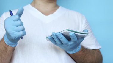 Tıp üniformalı bir doktor, tıp tarihini kağıda kalemle yazar. Mavi arka planda elinde kalem olan bir doktor. Tıbbi eldivenli doktor. Stüdyo video tıbbi