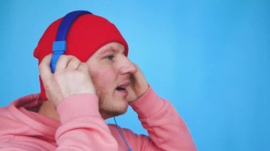 Gülümseyen, kırmızı şapkalı, mavi kulaklıklı, mavi kulaklıklı genç bir adam. Pembe renkli kapüşonlu, müzik kulaklıklı bir adam müzik dinliyor. Müzik favori konsepti.
