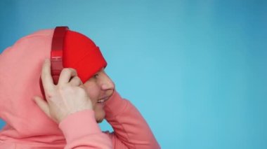 Ağır çekim. Müzik kulaklıklarıyla güzel bir gülümsemeyle müzik dinleyen genç bir adamın portresi. Bir adam en sevdiği müziği dinler ve gülümser. Stüdyo mavi arkaplan.