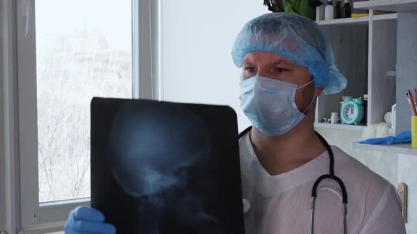 一位神经外科医生在医院的一个办公室里分析人的颅脑 医生手里拿着人类大脑的X光照片 医生分析颅骨损伤 疾病和伤害 — 图库视频影像