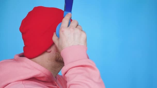 Счастливый Молодой Человек Красной Кепке Музыкальных Наушниках Синем Фоне Студии — стоковое видео