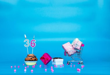 Kek pastası 36 'da mumları olan bir kız ya da kadın için doğum günün kutlu olsun. Mutlu yıllar pembe gözlüklü hediye kutuları. Mavi arkaplanda arkaplan kopyalama alanı yıldönümü.