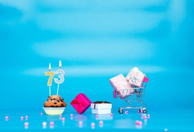 Yaratıcı kart 73 numaralı kek turtasında mumları olan bir kız ya da kadın için mutlu yıllar. Mutlu yıllar pembe gözlüklü hediye kutuları. Mavi arkaplanda arkaplan kopyalama alanı yıldönümü.