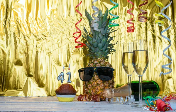 Cheerful pineapple in glasses festive happy birthday character with number  41. Beautiful background for congratulations copy space on a golden background with glasses of champagne. Anniversary congratulations with the number of candles burning with