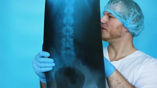 医者は病院のX線で人間の背骨を診断します 病院の医療従事者は 青い背景に肋骨のX線を分析します 病院の制服を着た男 健康コンセプト — ストック動画