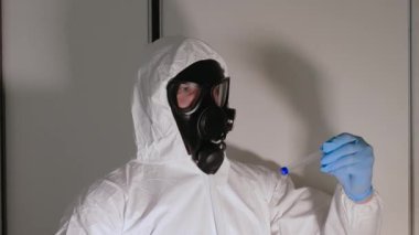 Kimyasal koruma altındaki bir kişi nesneler tarafından incelenir, gaz maskeli ve beyaz tulumlu bir adam, radyasyon salınımı. Kimyasal özelliklerin incelenmesi için laboratuvar