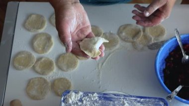 Yaşlı kadın hamurdan hamur köftesi ve krep heykeli yapıyor, mutfakta buğday unundan, yaşam tarzından yemek pişiriyor. Hamur köftesi heykeli. Ev yapımı gıda konsepti.