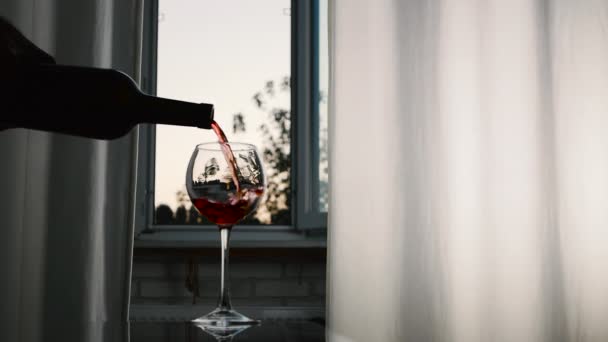 窓の背景に光沢のあるテーブルの上に赤ワインとワイングラス 日没時にグラスにワインを注ぐシルエット アロマティックワイン グラスにアルコール — ストック動画