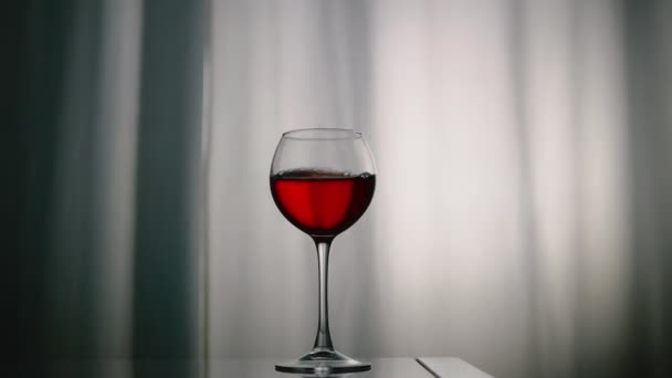 赤ワインがグラスに溢れています 光沢のあるテーブルの上のカーテンの背景に対するガラスの天然ワイン グラスでアルコールドリンクカルスニー — ストック動画