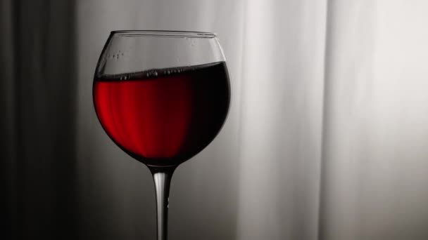 クローズアップ 風のカーテンの背景に対してグラスに赤ワイン ワイングラスにグレープワイン グラスにワインのシルエット アルコールドリンクレッド — ストック動画