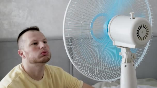 一个年轻人躲避炎热的天气 风扇子把人从炎热中冷却下来 风扇叶片在旋转 异常热 — 图库视频影像