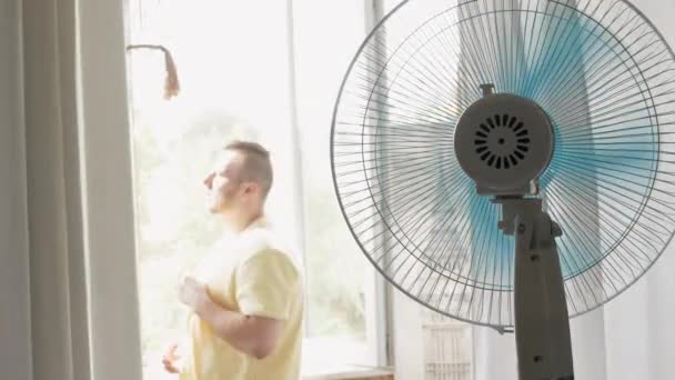 一个年轻人在公寓里被一个炎热的夏天的风扇冷却了 公寓内的风管风扇叶片 — 图库视频影像