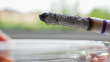 A cigarette smokes near the window, smoking a cigarette macro shot, on a gray bokeh background, a smoking cigar close-up. Extinguishing a cigarette butt in an ashtray.