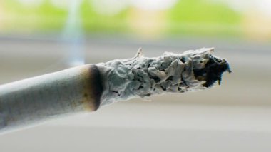 Bir sigara pencerenin yanında sigara içiyor, makro sigara içiyor, gri bir arka planda, yakın plan sigara içiyor..