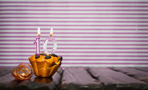 Birthday number 10. Date of birth with number of candles, copy space. Anniversary background with cake or muffin with burning candles. Greeting card.