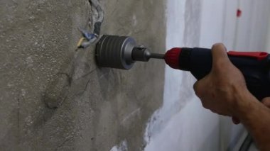 Beton duvarı delmek. Bir erkek işçi elinde matkapla duvarda bir oyuk açıyor. Daireye bir elektrik prizi kuruluyor.