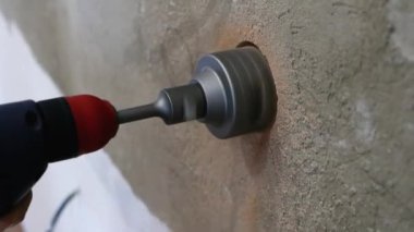 Tuğla bir duvara soket kutuları yerleştirmek. Bir erkek işçi elinde matkapla duvarda bir oyuk açıyor. Daireye bir elektrik prizi kuruyorum. İnşaat çalışmaları.