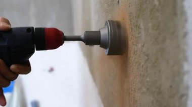 Tuğla bir duvara soket kutuları yerleştirmek. Bir erkek işçi elinde matkapla duvarda bir oyuk açıyor. Daireye bir elektrik prizi kuruyorum. İnşaat çalışmaları