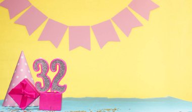 32 yaşında bir kızın doğum tarihi. Uzayı kopyala Sarı arkaplanlı pembe gözlüklü bir doğum günü. Üzerinde numaralandırılmış mumlar ve hediye kutusu olan dekorasyonlar. Bir kadın için yıldönümü kartı