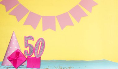 50 yaşında bir kızın doğum tarihi. Uzayı kopyala Sarı arkaplanlı pembe gözlüklü bir doğum günü. Üzerinde numaralandırılmış mumlar ve hediye kutusu olan dekorasyonlar. Bir kadın için yıldönümü kartı