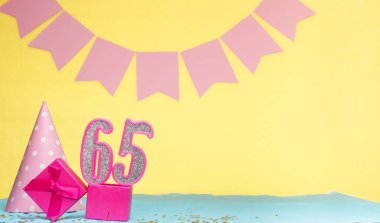 65 yaşında bir kızın doğum tarihi. Uzayı kopyala Sarı arkaplanlı pembe gözlüklü bir doğum günü. Üzerinde numaralandırılmış mumlar ve hediye kutusu olan dekorasyonlar. Bir kadın için yıldönümü kartı
