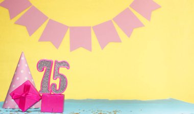 75 yaşında bir kızın doğum tarihi. Uzayı kopyala Sarı arkaplanlı pembe gözlüklü bir doğum günü. Üzerinde numaralandırılmış mumlar ve hediye kutusu olan dekorasyonlar. Bir kadın için yıldönümü kartı